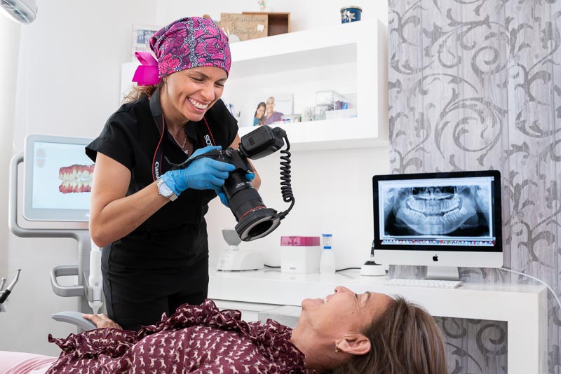 Dr. Maritza, dentist in Cancun at SOTA Dental, is taking a photograph of a middle-aged female patient. The dentist is holding the camera and smiling at the patient.