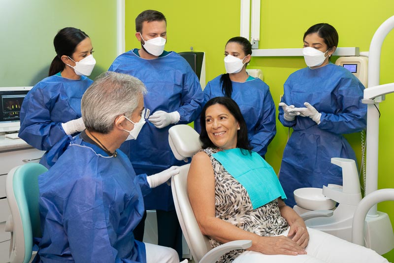 Dr. Mario, Dr. Alejandra, Dr. Gruber, and other dentists from SOTA Dental in Playa del Carmen are speaking with a female patient. She is smiling.