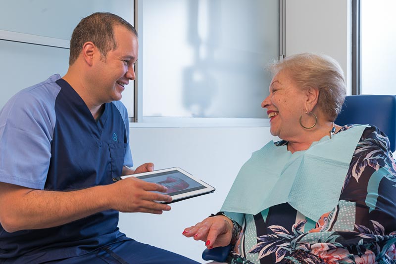 Dr. Bogarin, dentist at SOTA Dental in Tijuana, Mexico, speaks with an older female patient. He is using an iPad and they are both smiling.
