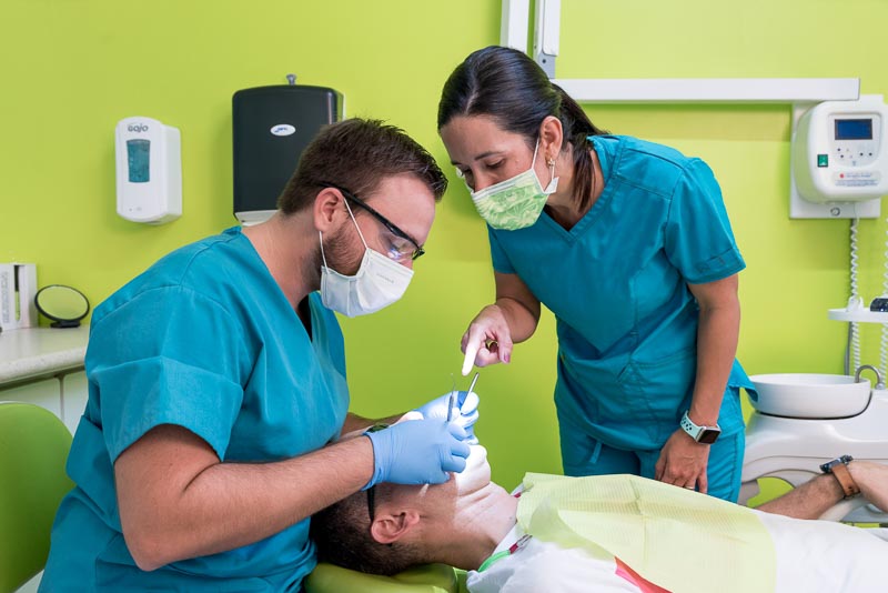 Dr. Alejandra and Dr. Gruber, dentists in Playa del Carmen, Mexico at SOTA Dental, perform dental work on a patient. Dr. Alejandra is pointing to the patients mouth while Dr. Gruber is working.