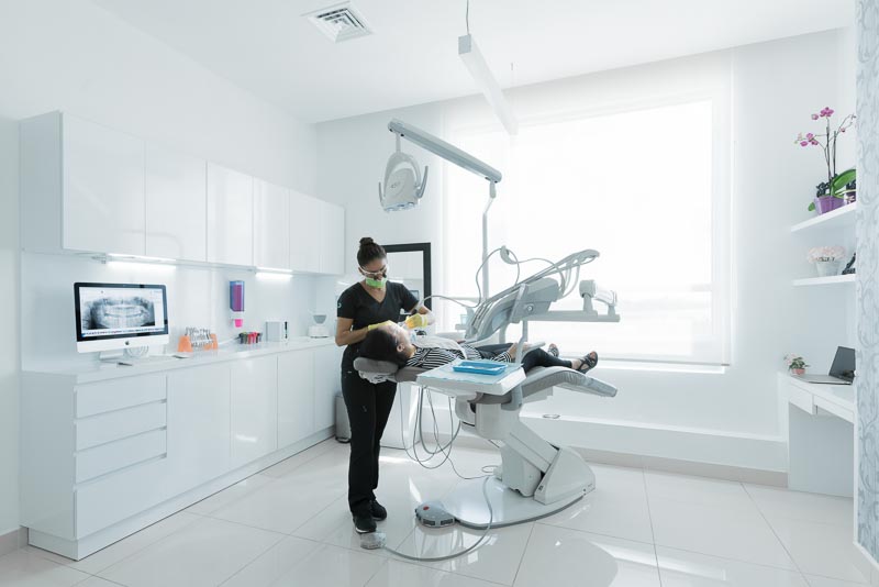 Dr. Maritza, dentist at SOTA Dental Cancun, is performing work in a large white dental room.
