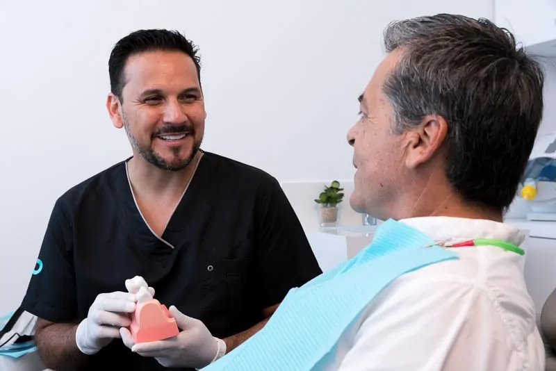 Dr. Omar, dentist in Cancun, Mexico at SOTA Dental, speaking with an older male patient about how to take care of dental implants. The patient is speaking and the dentist is listening and smiling.